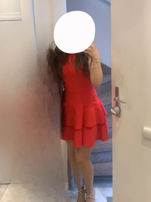 Röd volangklänning - Snygg röd kortklänning med volangkjol. Klänningen är ärmlös och har en figurnära passform som framhäver siluetten. Perfekt för dig som vill sticka ut med en färgstark look.