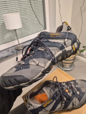 Merrell Continuum Ultra Sport waterpro Herrskor i Grå/Blå, Storlek 45 - Snygga kängor från Merrell i grått och svart med gula detaljer. Skorna har robust sula, ventilerande meshpaneler och snörning framtill. Perfekta för äventyr och outdoor. Märket syns tydligt på sidan och hälen. Materialmix av textil och syntet.