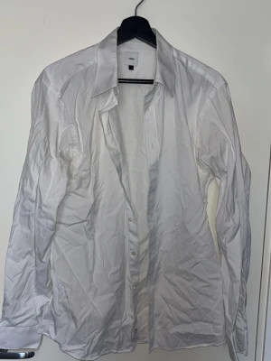 Vit klassisk skjorta från Bläck - Säljer en vit klassisk skjorta från Uniqlo med lång ärm och knappar framtill. Skjortan har en tidlös design med krage och är tillverkad i mjuk bomull. Perfekt att styla till olika outfits och funkar året runt.