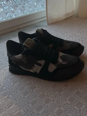 Valentino rock runners - Snygga svarta sneakers från Valentino med camomönster i grått och vitt. Skorna har en låg siluett, svarta snören och detaljer i mesh och mocka. Perfekta för dig som vill ha en cool och unik stil till vardags.