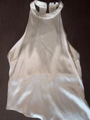 Champagnefärgad satin linnetopp - Snygg champagnefärgad linnetopp i satin med hög hals och ärmlös design. 