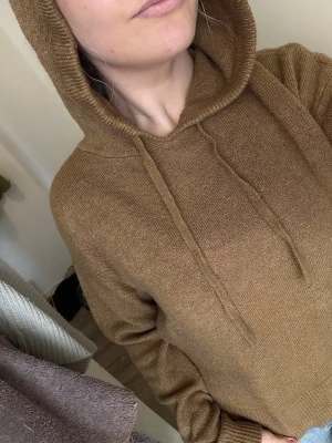 Brun stickad hoodie med huva - Säljer en snygg brun stickad hoodie med huva. Tröjan har ribbade muddar vid ärmslut och nederkant, och är tillverkad i ett mjukt stickat material. Nopprig, har liten fläck (kan nog tas bort). Tunt material.