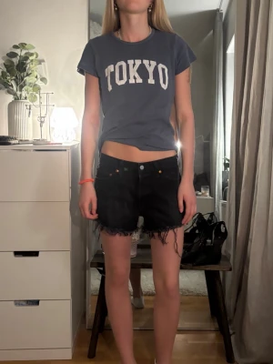Svarta jeansshorts från Levis - Snygga svarta jeansshorts med rå, fransig kant nertill och klassisk femficksdesign. Shortsen har en normal passform och är perfekta för varma dagar. Stängs med knapp och dragkedja framtill.