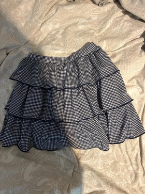 Rutig volangkjol från Zara - Supersöt kort volangkjol från Zara i blåvitt rutigt mönster. Kjolen har flera lager volanger som ger en lekfull och trendig look. Perfekt att matcha med en enkel topp för en cool outfit.