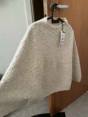 Krämvit stickad poncho från Gina Tricot - Mysig krämvit stickad poncho från Gina Tricot med grovstickad.