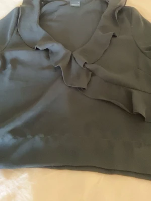 Svart blus med volangkrage - Stilren svart blus med volangkrage och långa ärmar. Ärmarna har knäppning vid mudden och blusen är tillverkad i ett tunt, flowy tyg. Jag har sytt upp den lite för att den var väldigt lång innan men den är ändå i ett bra skick. Den är ifrån Gina tricot i storlek 34💓💓