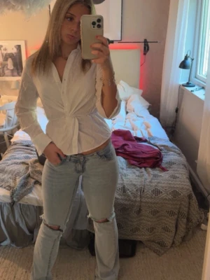 Vit twistad blus från Gina Tricot  - Snygg vit blus från Gina Tricot med twistad detalj i midjan och klassisk krage. Blusen har lång ärm och knappar framtill. Tillverkad i ett lätt och luftigt material som ger en avslappnad men stilren look.