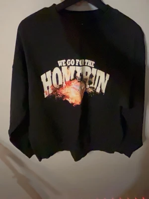 Svart hoodie med tryck 'HOMERUN' - Cool svart hoodie med trycket 'WE GO FOR THE HOMERUN' och en brinnande baseboll på bröstet. Oversized passform med rund hals och ribbade muddar. Perfekt för dig som gillar sportiga och streetinspirerade plagg.