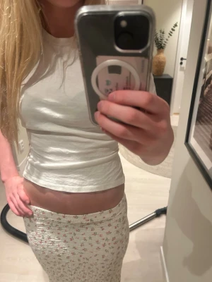 Vit croppad topp med öppen rygg - Snygg vit croppad topp med kort ärm och öppen rygg som knyts baktill. Perfekt för dig som gillar trendiga och unika detaljer. T-shirten har en enkel design framtill och cool knytning bak. Passar till både jeans och kjol.