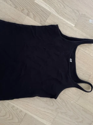 Svart linnetopp från H&M - En enkel och stilren svart linnetopp från H&M Basic, tillverkad i ekologisk bomull. Toppen har smala axelband och en klassisk passform som funkar till många olika looks.