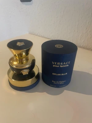 Versace Dylan Blue Pour Femme parfym - Versace Dylan Blue Pour Femme Eau de Parfum i en lyxig blå och guldig flaska med Medusa-detaljer. Flaskan har en rund, elegant form och kommer med originalförpackning. Innehåller 30 ml parfym. Ca 20ml kvar