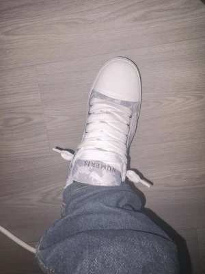 Gråvita  sneakers från NUMERIS - Snygga sneakers från NUMERIS i gråvitt camomönster med vita detaljer och grov sula. Skorna har vita snören, metallhål för snörningen och en tå i vitt läderliknande material. Perfekta för dig som gillar streetwear och vill sticka ut.