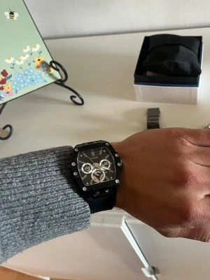 Svart klocka från Guess - Stilren svart klocka från Guess med fyrkantig urtavla och detaljer i silver. Klockan har en svart silikonrem och flera små urtavlor på insidan. Perfekt accessoar för dig som gillar modern design och tydliga detaljer.