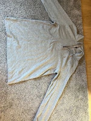 Grå långärmad tröja från Polo Ralph Lauren - Snygg grå långärmad tröja från Polo Ralph Lauren med halv dragkedja och klassisk broderad logga på bröstet. Tröjan är i mjukt bomullsmaterial och har en avslappnad passform. Perfekt för en stilren och bekväm look.