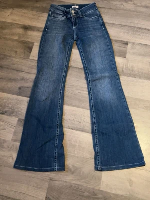 Blå bootcut jeans med broderade fickor - Snygga blå bootcut jeans med klassisk femficksdesign och broderade detaljer på bakfickorna. Jeansen har låg midja och utsvängda ben, perfekta för en avslappnad och trendig look. Tillverkade i denim med lätt tvättad finish.