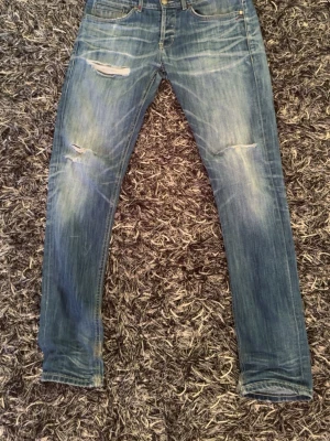 Blå slitna jeans från Dondup  - Säljer ett par blå jeans från Dondup med slitningar och hål på låren för en cool, avslappnad look. Jeansen har klassisk femficksdesign och raka ben. Perfekta för dig som gillar streetstyle och en trendig vibe. Storleken är 35 men passar till 31-33 om man bär det på andra jeans! Priset är ej hugget och kan diskuteras!
