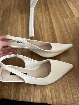 Beige pumps med öppen häl  - Stilrena pumps i beige med spetsig tå och öppen häl. Skorna har en smal klack och är tillverkade i ett slätt material som ger en elegant look. Perfekta för dig som gillar klassisk och trendig stil.