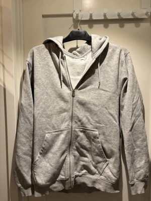 Grå zip-hoodie från Weekday | strl S - Snygg grå hoodie från Weekday med dragkedja framtill, huva med dragsko och två stora fickor. Tillverkad i mjukt sweatshirtmaterial som är perfekt för en avslappnad stil. Enkel och stilren design som funkar till det mesta.