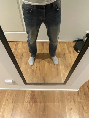Blå jeans - Säljer ett par blå slim/raka jeans från jack and jones med snyggt slitna detaljer och klassisk femficksmodell. Jeansen har en ljus tvätt med tydliga slitningar på lår och knän, samt gylf med knappstängning. Perfekta för en avslappnad och trendig look. Jeansen är lagade i skrevet men inget som syns eller känns när man har på sig de:)