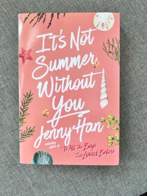 It's Not Summer Without You av Jenny Han - En ungdomsroman med rosa omslag, dekorerad med strandmotiv som snäckor och sjöstjärnor. Boken är på engelska och handlar om sommar, vänskap och kärlek. Perfekt för dig som gillar romantik och coming-of-age berättelser.