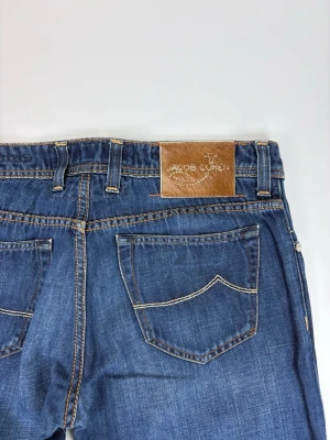 Blå jeans från Jacob Cohen - Snygga blå jeans från Jacob Cohen med klassisk femficksdesign och kontrastsömmar. Jeansen har rak passform och läderpatch med logga bak i midjan. Tillverkade i mjuk denim med en stilren look.