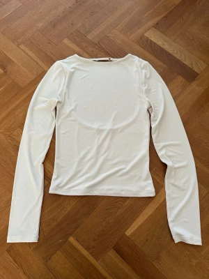 Vit långärmad topp med öppen rygg - Stilren vit långärmad topp med rund halsringning och en stor öppen ryggdetalj. Tillverkad i ett mjukt och stretchigt material som ger en slim passform. Perfekt för att skapa en clean och trendig look.