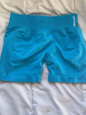 Electric blue impact shorts DFYNE - Snygga turkosa seamless shorts från DFYNE med hög midja och ribbad linning. Perfekta för träning eller chill, med stretchigt material som sitter skönt och formar sig efter kroppen. Logga på linningen både fram och bak.