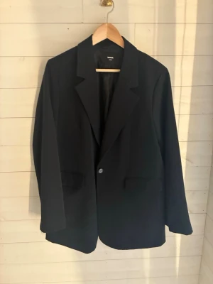 Svart klassisk kavaj från bikbok - Stilren svart kavaj från bikbok med enkelknäppning och två fickor framtill. Klassisk passform med slag och helfodrad insida. Perfekt för en clean och tidlös look. 