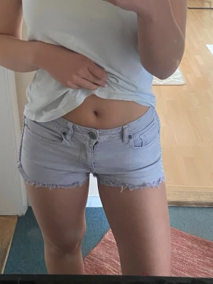 Ljusgrå jeansshorts med flätad detalj - Säljer ett par ljusgrå jeansshorts med fransig kant och snygg flätad detalj längst sidorna! Från Kendall & Kylie, storlek 5, men är som Xs/s