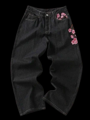 Svarta jeans med broderade blommor - Unika svarta jeans med bred passform och snyggt broderade rosa körsbärsblommor på ena höften och bakfickan. Jeansen har klassisk femficksdesign och är tillverkade i kraftigt denimtyg. Perfekta för dig som vill sticka ut med coola detaljer.