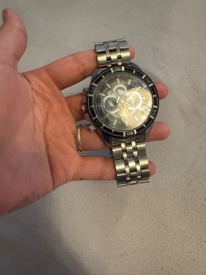 Stilren silverfärgad herrklocka - Snygg herrklocka i silver med metallarmband och svart urtavla. Klockan har flera små urtavlor och tydliga siffror runt boetten. Perfekt accessoar för dig som gillar en klassisk och stilren look.