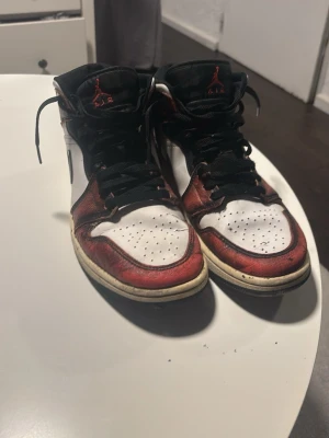 Air Jordan 1 Retro mid röd/vit - Säljer ett par klassiska Air Jordan 1 Retro mid i färgerna röd, vit och svart. Skorna har svart swoosh, svarta skosnören och hög siluett. Ovandelen är i läder med perforerad tåbox och ikonisk Jumpman-logga på plösen. Finns lite slitningar efter användning men inte extrema utan dem på bild.
