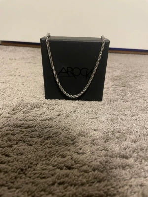 Silverfärgat repkedjehalsband AROCK - Snyggt halsband från AROCK i silverfärg med repkedja. Kedjan har en tvinnad design som ger en cool och modern look. Perfekt accessoar för att lyfta din outfit. Lås i metall och stilren finish.