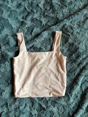 Beige croppad topp från Amisu - Snygg croppad topp från Amisu i beige färg med breda axelband och fyrkantig halsringning. Perfekt att matcha med höga jeans eller kjol för en trendig look.