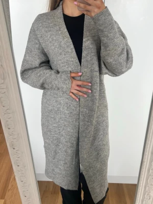 Kofta - Lång, öppen grå kofta med beiga inslag i mjuk stickad kvalitet. Koftan har långa ärmar, ribbade muddar och en avslappnad passform. Supermysig 💕 Storlek XS från H&M. Lite nopprig men har mer att ge 🩷