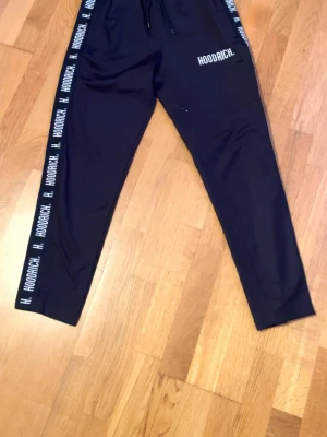 Hoodrich Mjukisbyxor Svarta (ny skick) - Svarta mjukisbyxor från Hoodrich med vita logotyper längs sidorna och tryckt logga på ena låret. Byxorna har dragsko i midjan och smal passform. Perfekta för en avslappnad streetwear-look. Storlek S passar XS-M. Nyskick