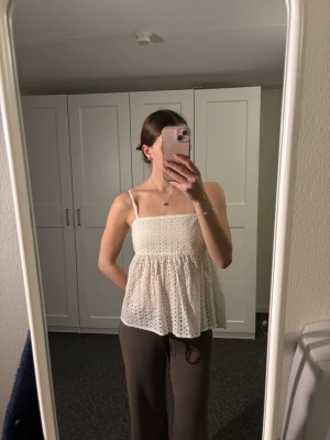 Vit broderad linnetopp från BikBok - Säljer en söt vit linnetopp från BikBok i storlek S. Toppen har tunna axelband, smock upptill och ett broderat mönster över hela plagget. Den är lätt utsvängd nedtill och perfekt för varma dagar. Superfin att styla med jeans eller kjol!