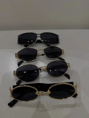 Fyra par trendiga solglasögon - Säljer fyra par solglasögon i olika former. Tre har guldfärgade metallbågar och svarta glas, en har helsvart båge. Bågarna är ovala och runda med coola detaljer. Perfekta accessoarer för att lyfta din stil.