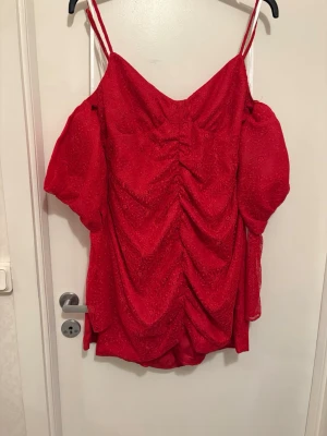 Röd omlottklänning med puffärm - Klänning från Lovers and Friends. Snygg röd kortklänning med tunna axelband och puffiga ärmar. Klänningen har omlottdetalj och är gjord i ett spetsliknande material med blommigt mönster. Perfekt för dig som vill sticka ut med en färgstark look.