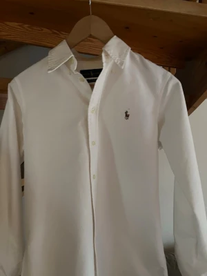 Vit skjorta från Ralph Lauren - Klassisk vit skjorta från Ralph Lauren med custom fit och broderad logga på bröstet. Skjortan har jag använt en gång på ett dop testa den nu och den var för liten inga fläckar eller slitage. Perfekt för en clean och stilren look inför sommaren. Tveka ej med frågor! (Pris kan diskuteras)