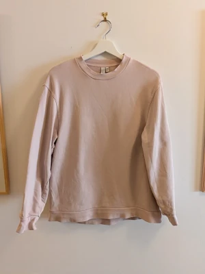 Ljusbeige sweatshirt från & Other Stories - En stilren ljusrosa sweatshirt från & Other Stories med rund halsringning och långa ärmar. Tillverkad i mjukt bomullsmaterial och har en relaxed fit som passar perfekt till jeans eller kjol. Enkel och clean design utan tryck eller mönster.