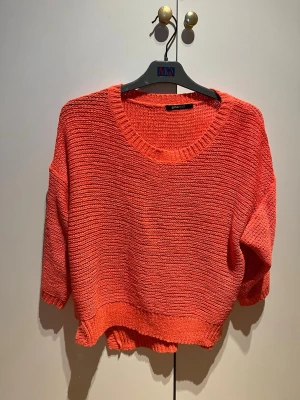 Korall stickad tröja  - Säljer en korall förgad stickad tröja med rund halsringning och trekvartsärmar. Tröjan har en avslappnad passform och ribbstickade detaljer vid hals, ärmslut och nederkant. Perfekt för att addera färg till din outfit.