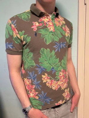 Blommig Ralph Lauren piké – M Custom Slim Fit - Säljer en unik blommig Ralph Lauren piké i custom slim fit, storlek M. Perfekt för en somrig och stilren look. I fint skick.  Har du frågor? Tveka inte att höra av dig. Allt gott från Deluxe garderoben ⭐️