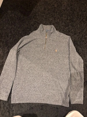 Grå halvzip-tröja från Polo Ralph Lauren - Snygg gråmelerad halvzip-tröja från Polo Ralph Lauren med klassisk broderad logga på bröstet. Tröjan har hög krage med dragkedja och är tillverkad i mjukt material. Perfekt för lager-på-lager och stilren look. Priset är såklart inte hugget i sten! Nypris 2800kr.