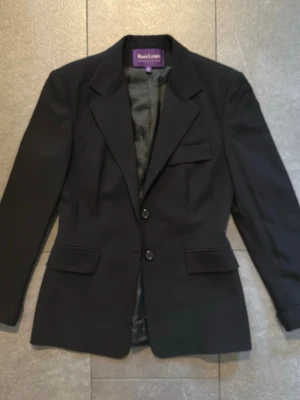 Purple Label Ralph Lauren kavaj - Svart - Dam storlek 8 - Exklusiv svart kavaj från Ralph Lauren Purple Label, tillverkad i Italien i 100% ull med snygg klassisk passform som passar både vardag och mer uppklädda tillfällen. Kavajen är i mycket fint skick och har två knappar framtill. Köpt second hand, alla detaljer stämmer väl överens med Ralph Lauren Purple Label, säljs utan kvitto.