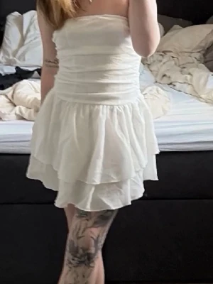 Vit axelbandslös volangklänning - Supersöt vit kortklänning med volangkjol och smockad överdel. Axelbandslös design som ger en clean och fräsch look.💕                         Den passade inte mig så bra så säljer vidare deno . Den har inga fläckar men behöver strykas/ ångas💕