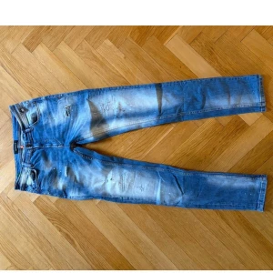 Blå slitna jeans - Säljer ett par blå  jeans med slitningar och blekta detaljer. Jeansen har klassisk femficksdesign och låg midja. Perfekta för en avslappnad och trendig stil.