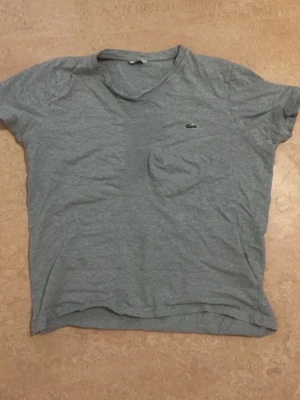 Grå t-shirt från Lacoste - En basic grå t-shirt från Lacoste med klassisk krokodillogga på bröstet. T-shirten har rund halsringning och korta ärmar. Perfekt för en avslappnad och stilren look.