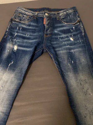 Blå slitna jeans från Zara  - Säljer ett par blå jeans från Zara med coola slitningar och distressed detaljer. Jeansen har klassisk femficksmodell, orange sömmar och en röd logotagg vid gylfen. Perfekt för dig som gillar en trendig och avslappnad stil.
