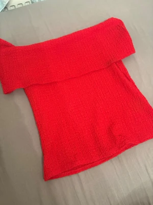 Röd offshoulder topp från H&M - Trendig röd offshoulder topp från H&M i stretchigt, strukturerat material. Toppen är axelbandslös och har en croppad passform som passar perfekt till höga jeans eller kjol. Enkel men snygg design som sticker ut med sin starka färg.